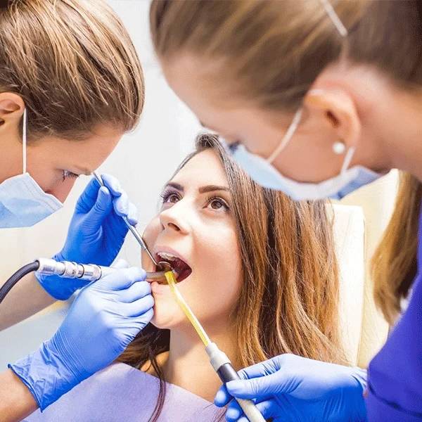 Dental professionals in protective gear examine patient's teeth during a dental appointment in a clean clinical setting